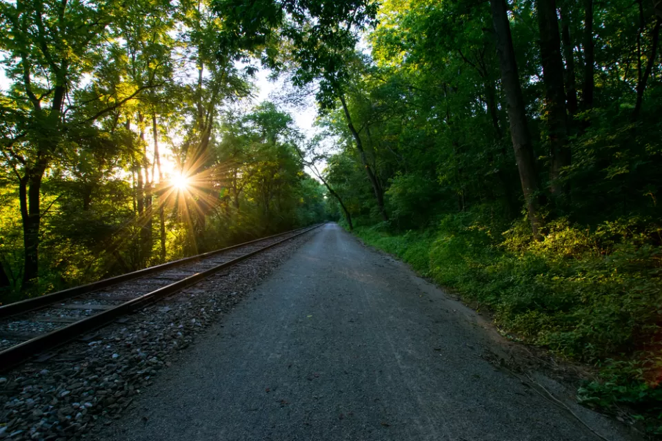 Heritage Rail Trail County Park, York, Pennsylvania with railroad next to unpaved walking/biking trail and sun filtering through green trees